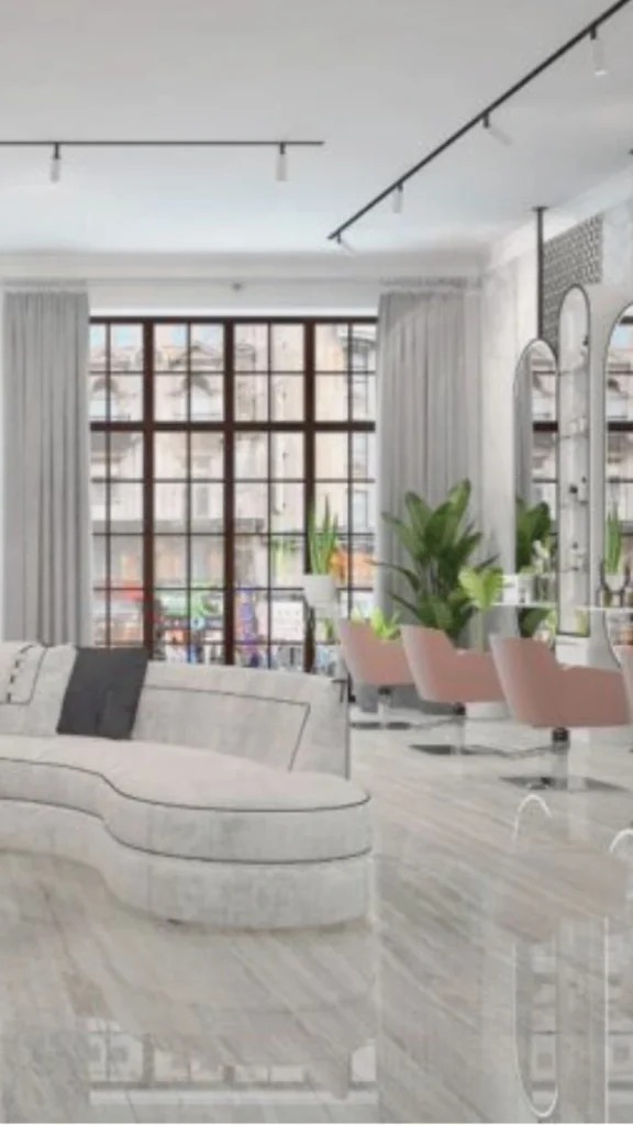 A bright and elegant luxury hair studio designed with a sophisticated neutral color palette. In the foreground, a curved, modern off-white sectional sofa with dark contrast piping sits on a glossy, light gray marble floor that mirrors the room's elements. To the right, stylish dust-pink or blush styling chairs face tall, arched mirrors. The far wall features a massive, floor-to-ceiling black-framed grid window covered with sheer grey curtains, revealing a city street view outside. Potted tropical green plants add a natural element, while clean black industrial track lighting lines the white ceiling.