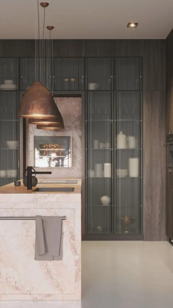 A sleek, ultra-luxury modern kitchen focusing on a premium material palette and high-end appliance integration. In the foreground, a massive island is wrapped completely in a polished pink-toned marble with subtle reddish veins, featuring an integrated prep sink with a matte black faucet. Hanging directly above the island are three iconic, low-profile dome pendant lights finished in heavily textured, hammered copper. The background features floor-to-ceiling dark wood cabinetry seamlessly integrated with smoked glass display doors featuring fine vertical reeding, revealing softly illuminated shelves.