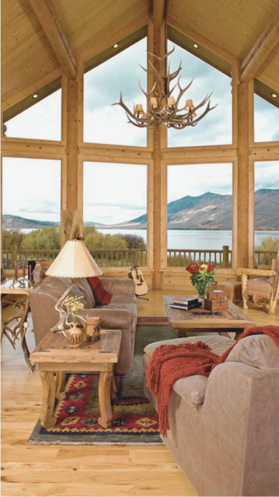 A close-up of a meticulously layered seating area within an elegant lodge interior, emphasizing contrasting natural textures. A plush, cream-colored armchair upholstered in a soft, low-pile boucle fabric is decorated with a chunky, hand-woven taupe throw blanket and a smooth, dark brown leather accent pillow. Resting on a dark-stained wood floor, a thick, natural jute area rug anchors the layout, while a smooth, minimalist ceramic vase holding delicate dried botanicals sits on a nearby rustic side table, demonstrating a curated and tactile aesthetic where texture does the talking.
