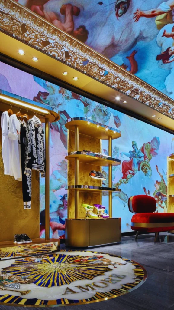 A luxury jewelry store interior showcasing an expert combination of layered retail lighting. Targeted overhead cylinder spotlights illuminate a continuous glass-top wooden display counter, while warm hidden LED strip lighting sculpts the interior of teal-colored, arched wall niches. The illuminated niches showcase premium necklaces on bust displays, while a wall of mirrors reflects the sophisticated space and modern grey upholstered barstools.