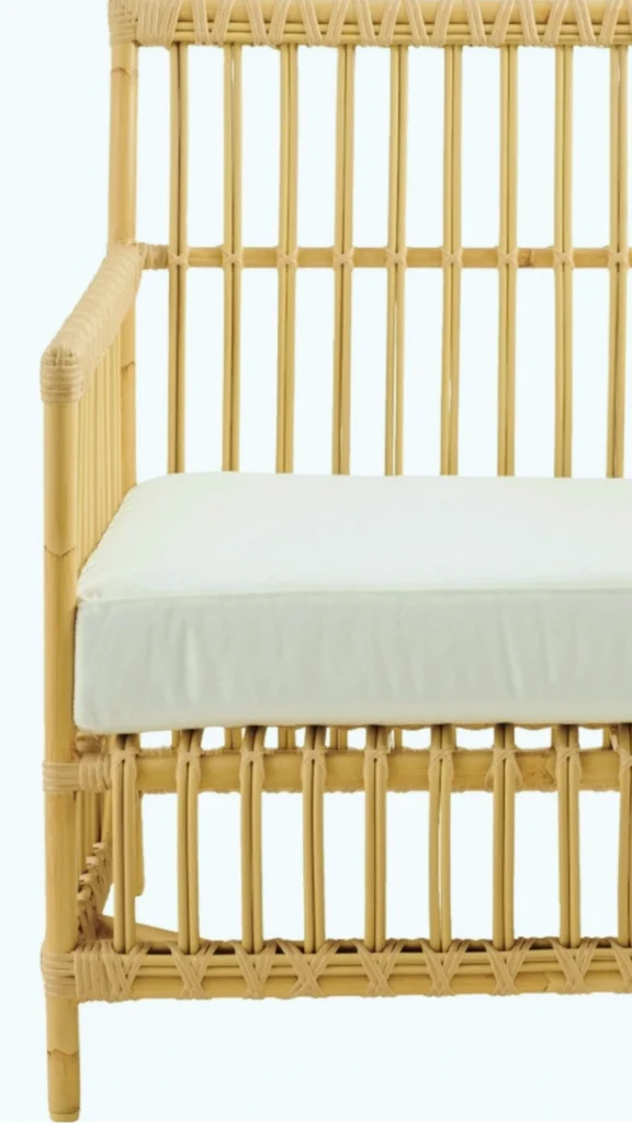 A sustainable luxury furniture piece showcasing an open, mass-reducing frame that perfectly blends timeless design with modern ecology. The high-backed bench or armchair features a beautifully structured frame crafted from natural light bamboo or rattan poles, arranged in a clean, vertical openwork grid. A thick, minimalist cream-colored cushion with a removable cover rests on the seat, emphasizing timeless simplicity and repairable luxury.