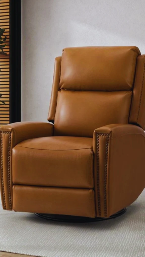 A sophisticated luxury seating design featuring a modern swivel lounge armchair. The chair is expertly tailored in a smooth, warm caramel-brown leather and detailed with classic antiqued bronze nailhead trim running down the face of the armrests. It sits on a hidden, low-profile 360-degree rotating swivel ring base on a textured cream area rug, epitomizing kinetic, fluid geometry for open-concept layouts.