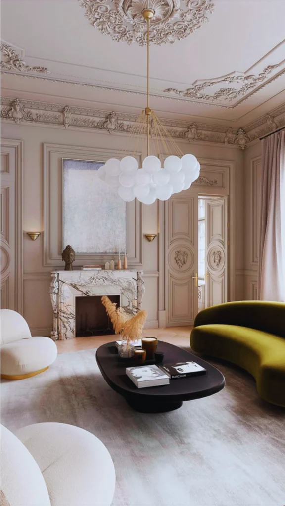 A stunning neo-classical luxury room where classic architecture meets contemporary furniture silhouettes. A sleek, curved olive-green velvet sofa and rounded ivory bouclé armchairs introduce bold modern geometry into a space adorned with historic details, including an ornate marble fireplace, intricate wall paneling, and a highly decorative ceiling medallion. Hanging above is a playful, modern cloud-like bubble chandelier that creates beautiful character and tension.