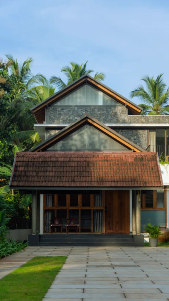 A luxury modern tropical villa showcasing a stunning fusion of sleek contemporary walls and elegant sloped roofs. The architectural design features three tiers of steeply pitched gabled roofs, including a prominent front entryway canopy laid with classic reddish-brown terracotta clay tiles. The upper gables incorporate translucent ribbed glass panels and warm wood accents, creating a dignified silhouette against a backdrop of lush green palm trees.