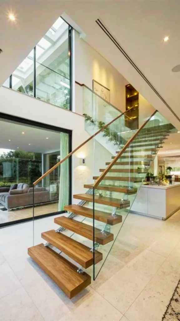 A premium floating staircase featured in a modern, open-plan luxury home to showcase the future of interior design. The structure highlights thick, natural wood steps that appear to suspend in mid-air, supported underneath by clean metallic brackets. A minimalist, seamless glass balustrade with a sleek wooden handrail encloses the flight, preserving interior sightlines and allowing natural daylight from the upper floor windows to flood the open living space.