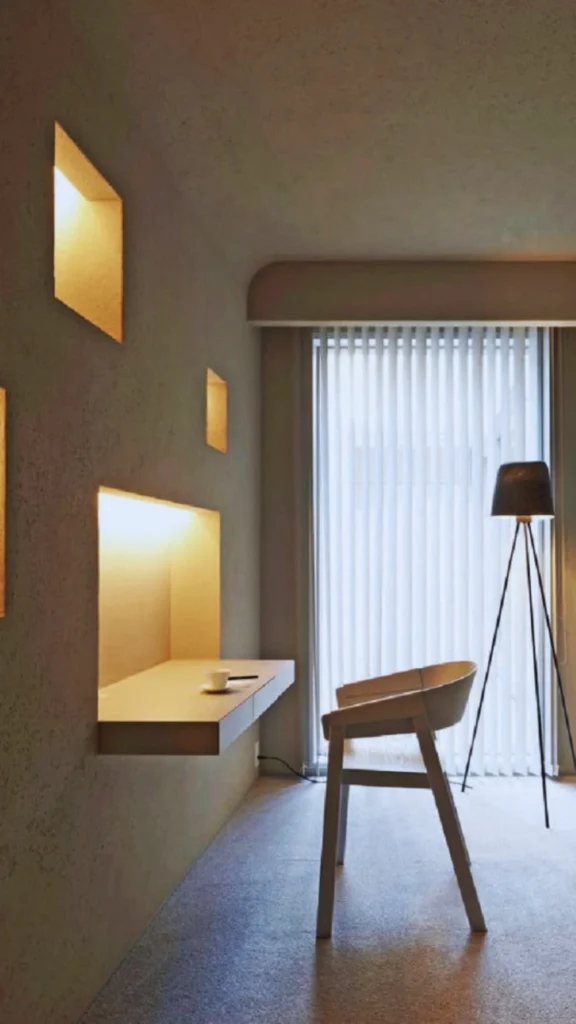 A luxury modern living room showcasing an automated human-centric lighting design shifting to a warm evening setting. Linear LED cove lighting runs along the top of a smooth vertical oak wood accent wall, casting a soft, indirect golden glow over a large curved cream sectional sofa. The tranquil ambiance supports the body's natural circadian rhythm, complemented by a tall fiddle-leaf fig plant, a neutral area rug, and stone coffee tables.